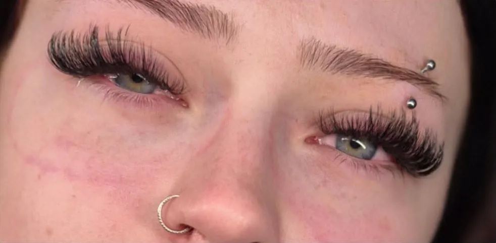 A smiling client with green eyes showing a full, wispy set of lash extensions
